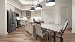 A modern kitchen with a central island, stainless steel appliances, pendant lighting, and a dining area with chairs. - Landing | Chic 2BD, Gym (Austin)