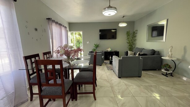 A modern living room with a dining area, grey sofas, a flat-screen TV, and a fireplace. - Comfortable 2BR Condo in Sosúa w/ AC Near Beaches (Sosúa)