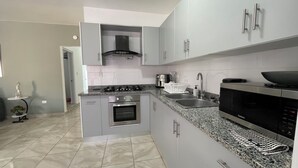 A modern kitchen with grey cabinets, a built-in oven, a microwave, and a granite countertop. - Comfortable 2BR Condo in Sosúa w/ AC Near Beaches (Sosúa)