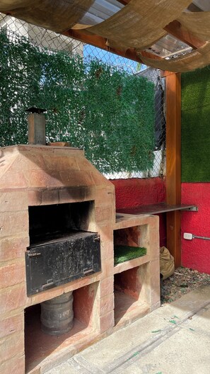 A brick-built outdoor oven with a chimney, a wooden shelf, and a red wall in the background. - Comfortable 2BR Condo in Sosúa w/ AC Near Beaches (Sosúa)