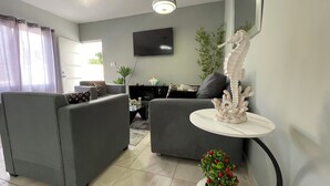 A living room with grey sofas, a flat-screen TV, a decorative seahorse sculpture, and a small potted plant. - Comfortable 2BR Condo in Sosúa w/ AC Near Beaches (Sosúa)