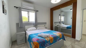 A bedroom with a bed, a nightstand, a dresser, an air conditioning unit, a window with curtains, and a mirror. - Comfortable 2BR Condo in Sosúa w/ AC Near Beaches (Sosúa)