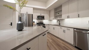 A modern kitchen with a central island, stainless steel appliances, and light wood cabinetry. - Landing | Chic 2BD, Gym (Austin)