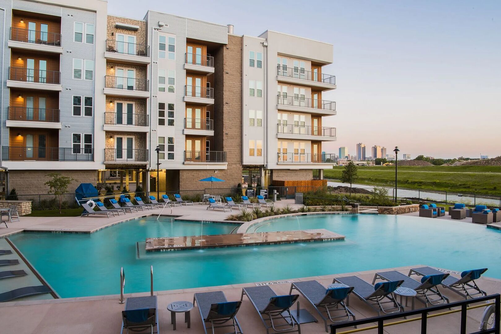 A modern hotel with a pool area, multiple balconies, and a view of the city skyline.