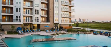 A modern hotel with a pool area, multiple balconies, and a view of the city skyline.