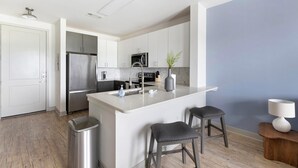 A modern kitchen with stainless steel appliances, a white island with stools, and a blue accent wall.