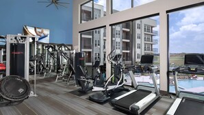Une salle de sport moderne, dotée de divers équipements d’exercice, de grandes fenêtres et offrant une vue sur un immeuble d’habitation.