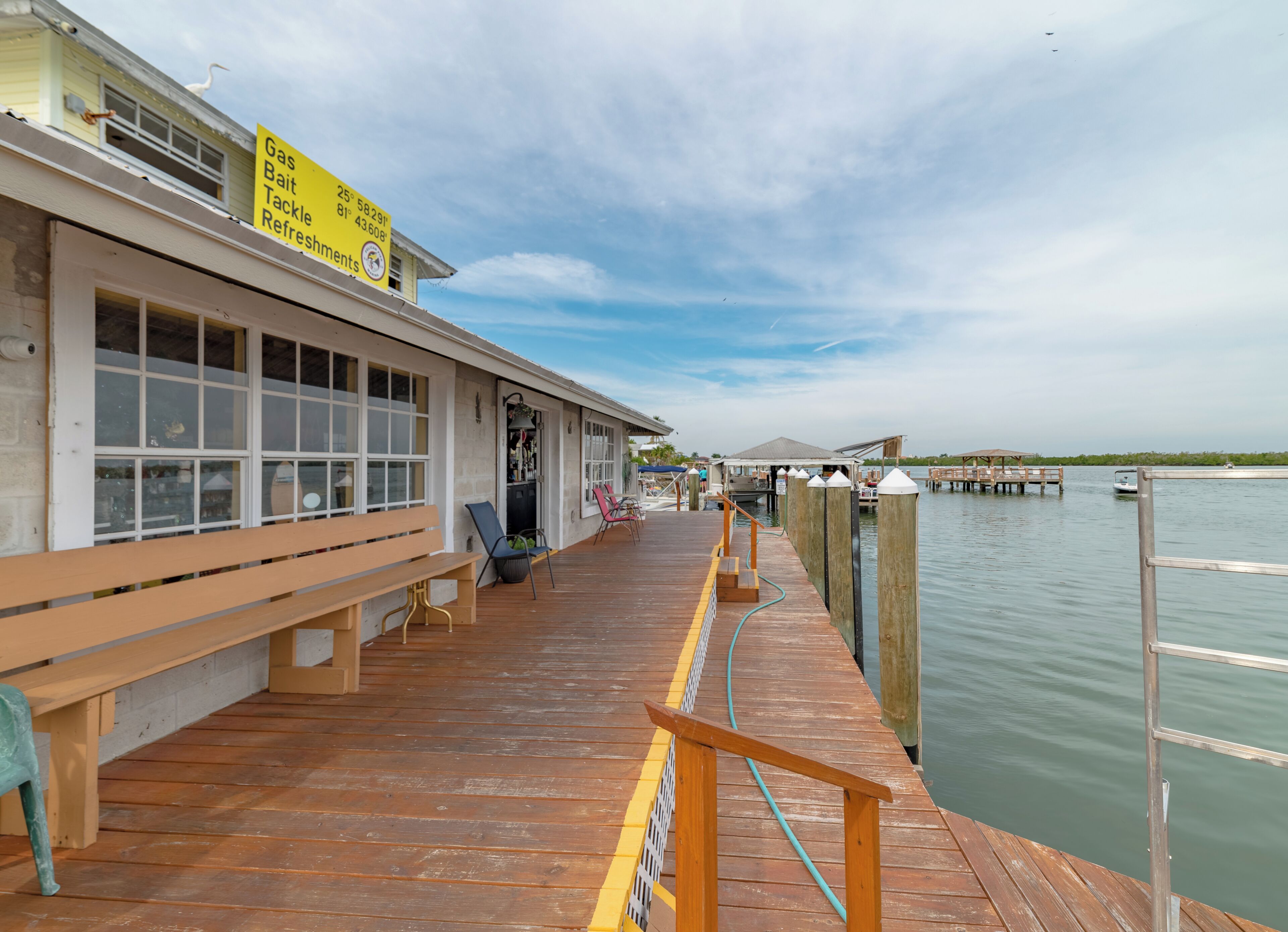 A wooden pier leading to a dock with a building featuring large windows and a bench.