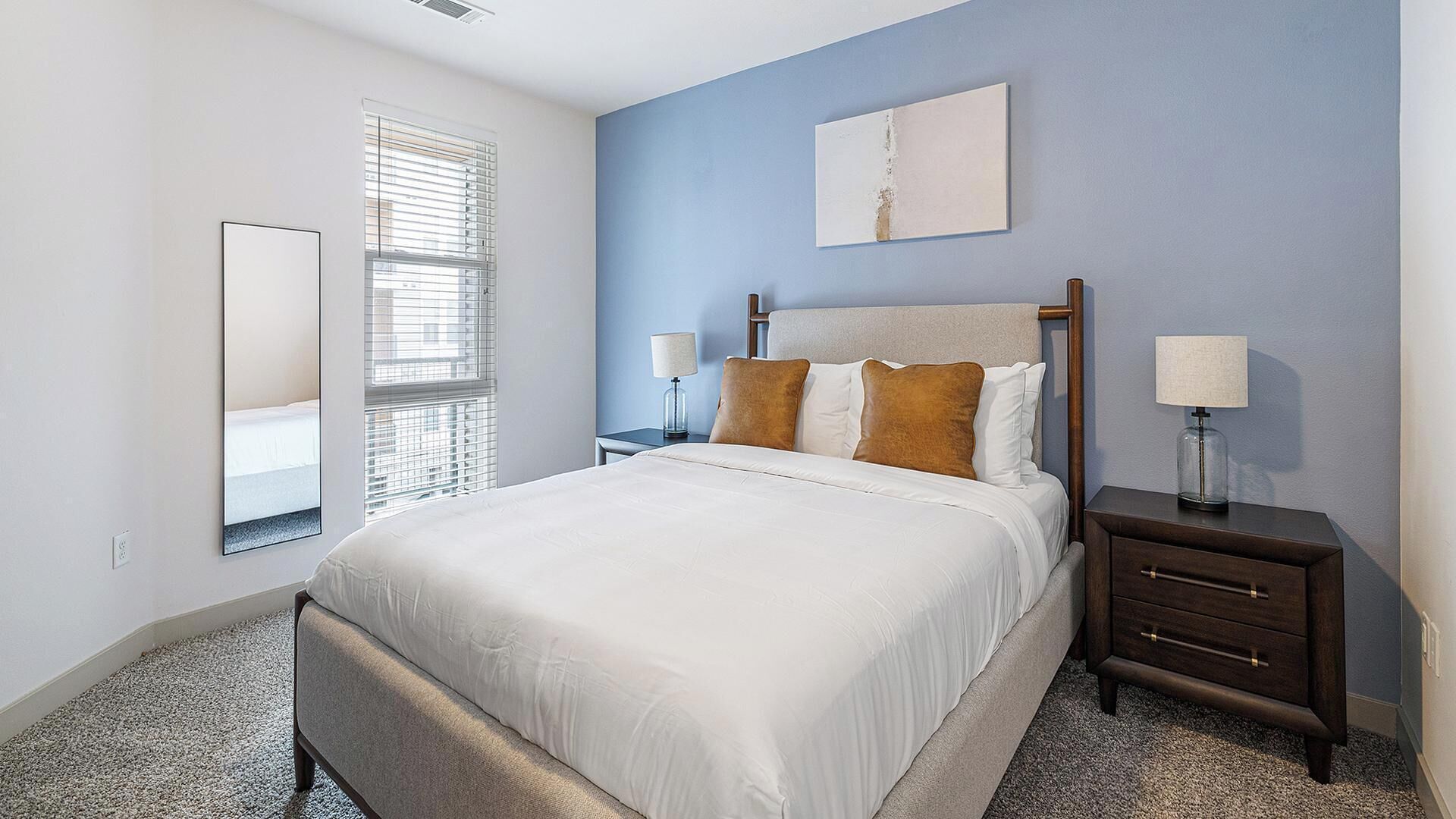 A bedroom with a bed, bedside tables, a mirror, and a painting on the wall.