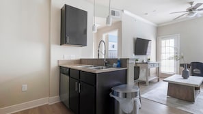 A modern kitchen with a dishwasher, double sink, and a small trash can. - Landing | Modern 1BD, Gym (Austin)