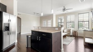 A modern kitchen with a stainless steel refrigerator, a granite countertop, and a ceiling fan. - Landing | Modern 2BD, Gym (Austin)