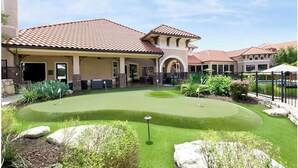 A residential area with a house, a patio, and a small putting green. - Landing | Amazing 2BD, Gym (Austin)