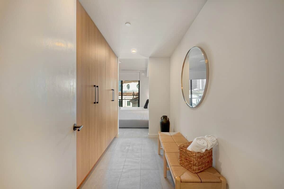 A hallway with a wooden wardrobe, a bench with towels, and a round mirror on the wall.