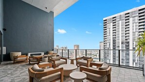 Un salón en la azotea con mobiliario exterior, vistas a la ciudad y un rascacielos al fondo.