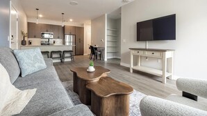 Ein modernes Wohnzimmer mit Sofa, Couchtisch, Fernseher und einer Küche im Hintergrund.
