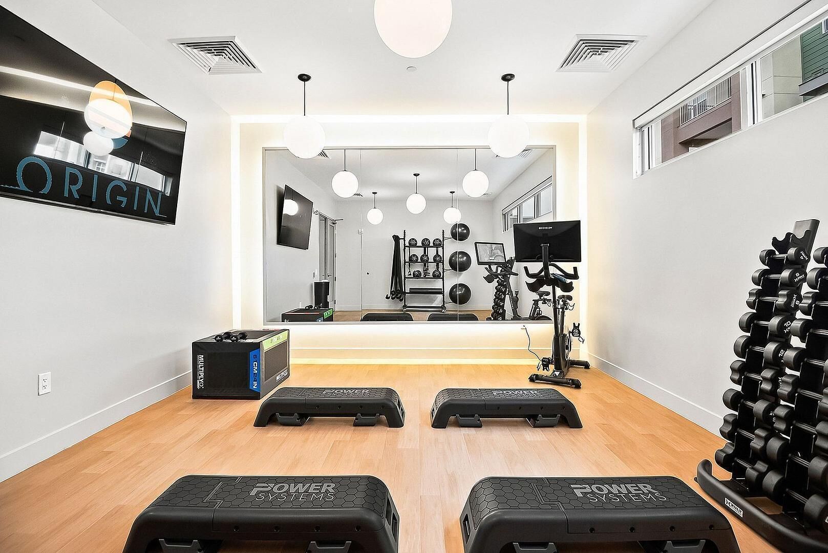 A home gym with exercise equipment, a treadmill, and a mirror reflecting the room.