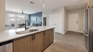 A modern kitchen with a large island, stainless steel appliances, and a view to the dining area. - Landing | Incredible 3BD, Pool, Clubhouse (Goodyear)