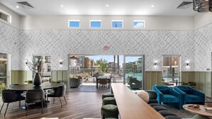 A modern hotel lobby with a long wooden reception desk, comfortable seating areas, and a view of the outdoor patio. - Landing | Amazing 2BD, Pool, Gym (Goodyear)