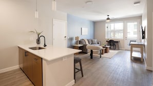 A modern kitchen with a central island, a dining area with a table and chairs, a sofa, and a large window. - Landing | Amazing 1BD, Clubhouse, Gym (Goodyear)