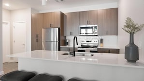 A modern kitchen with a central island, stainless steel appliances, and wooden cabinetry. - Landing | Amazing 1BD, Clubhouse, Gym (Goodyear)