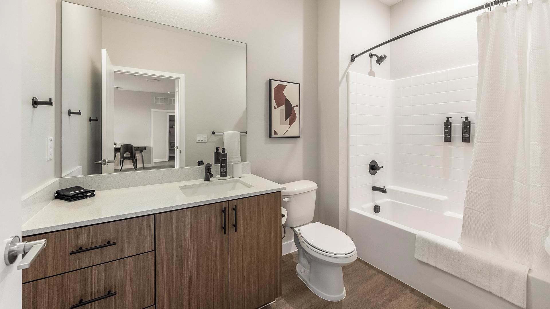 A modern bathroom with a large mirror, a toilet, a shower with a curtain, and a vanity with a sink and cabinets.