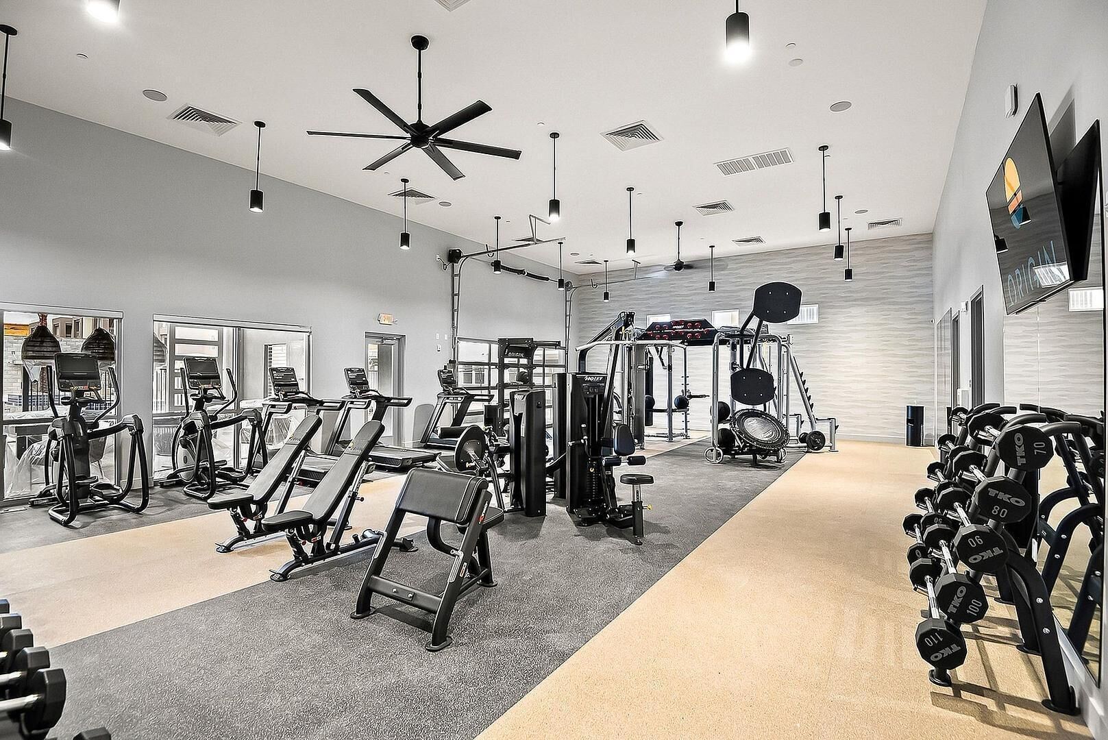 Une salle de sport équipée de divers appareils d’exercice, de ventilateurs de plafond et d’un écran de télévision.