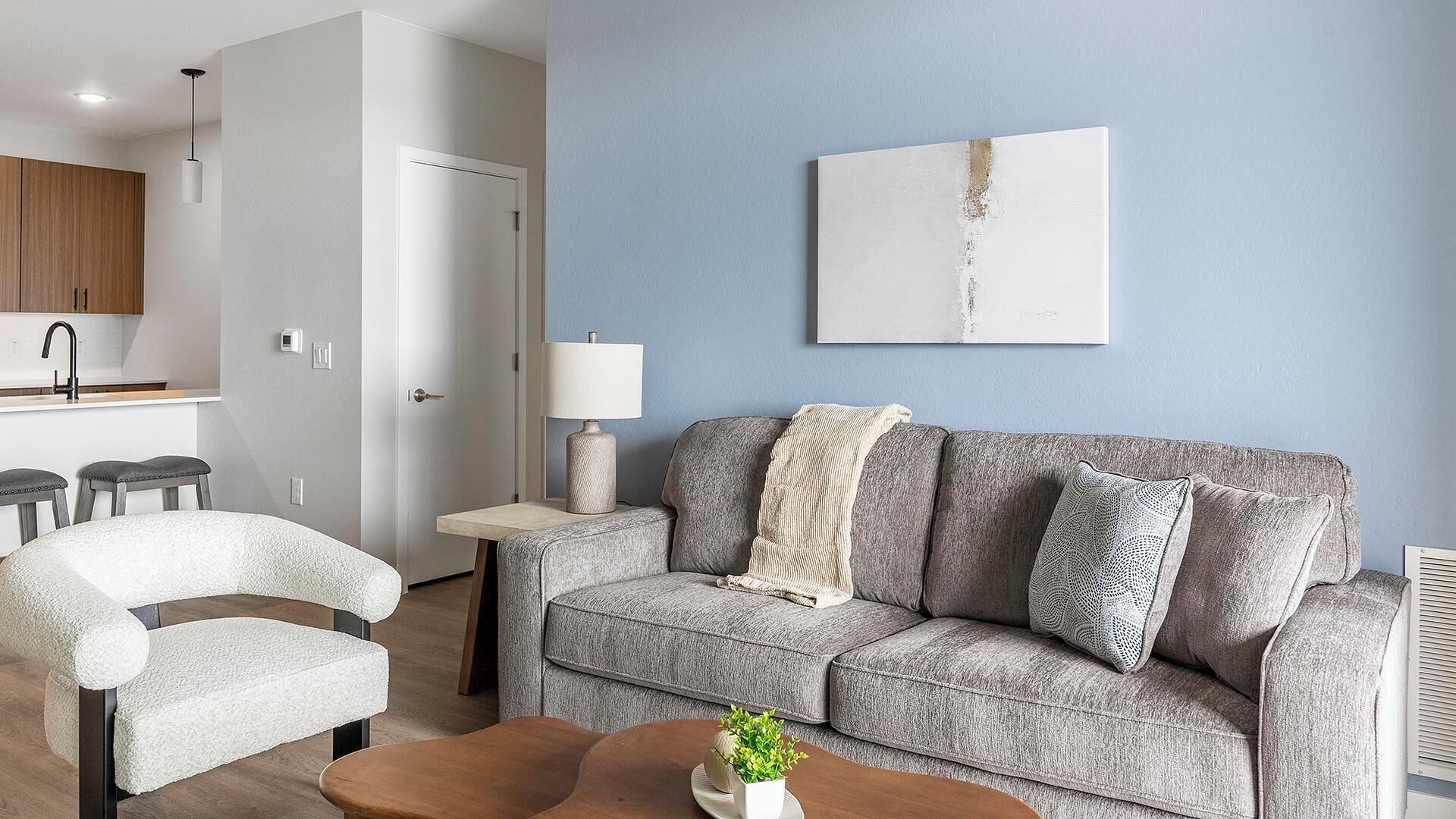 A living room with a grey sofa, a white armchair, a wooden coffee table, and a small plant.