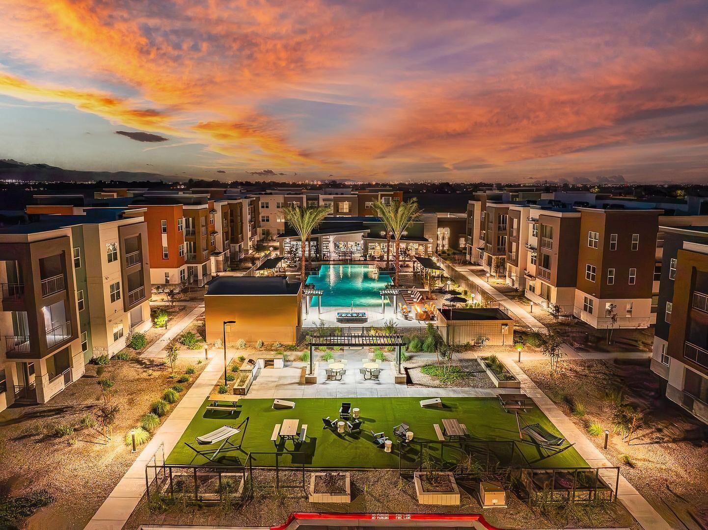 Um moderno conjunto de apartamentos com piscina central, área de estar externa e gramado bem cuidado.