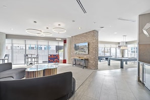 A modern lounge area with a pool table, comfortable seating, and a brick accent wall.