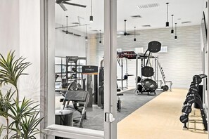 A modern gym with exercise equipment, a 'FITNESS' sign, and a large window. - Landing | Modern 1BD, Pool, Clubhouse (Goodyear)