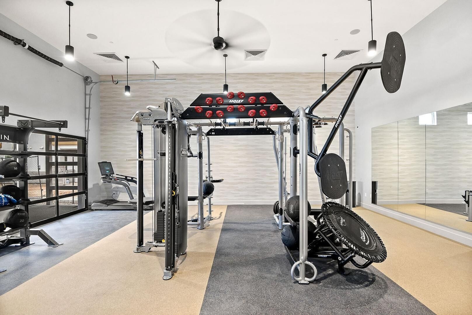 A gym with a weightlifting station, a treadmill, and a mirrored wall.