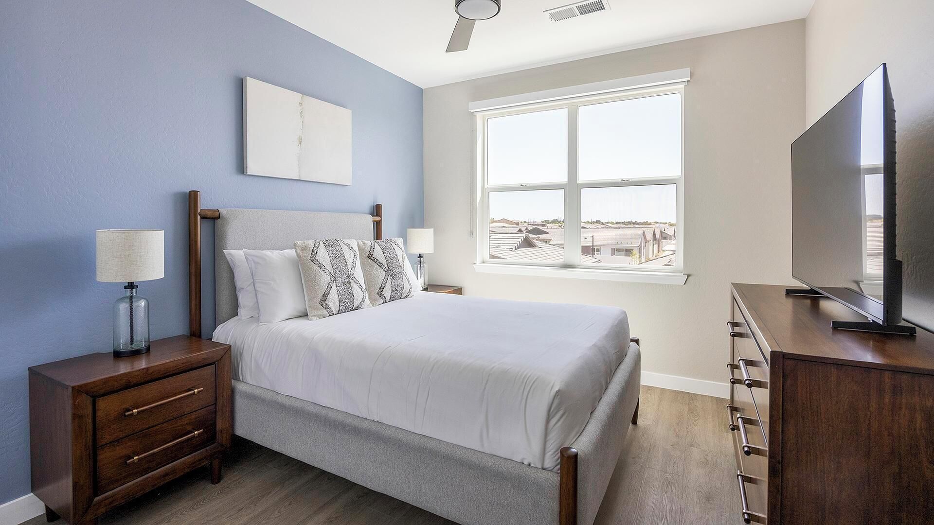 A bedroom with a bed, nightstands, a TV, and a window with a view.