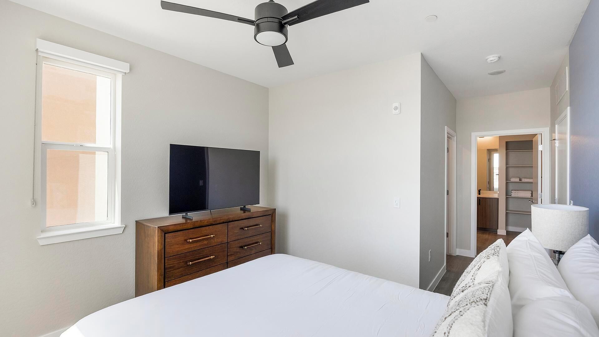 A bedroom with a bed, a TV on a dresser, a ceiling fan, and a closet.