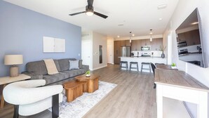A modern living room with a sofa, coffee table, and a TV. - Landing | Chic 2BD, Clubhouse, Gym (Goodyear)