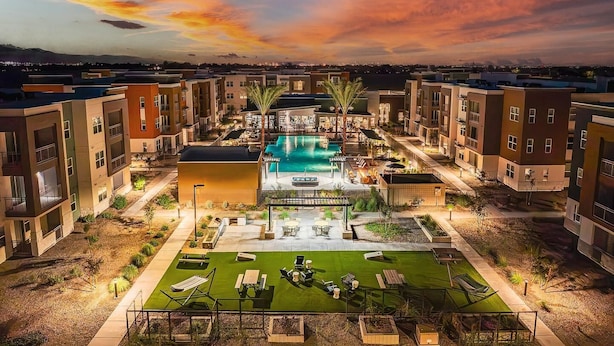 A modern apartment complex with a central swimming pool, outdoor seating, and a well-maintained lawn. - Landing | Amazing 1BD, Gym, Pool (Goodyear)