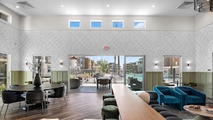 A modern hotel lobby with a long wooden reception desk, comfortable seating areas, and a view of the outdoor patio. - Landing | Amazing 1BD, Gym, Pool (Goodyear)