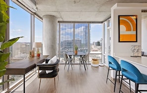 A modern office space with a large window, a table with chairs, a bar area, and a view of the cityscape. - Work-Ready Downtown Stay | Rooftop Lounge & Kitchen | Near Broadway & Symphony (Nashville)