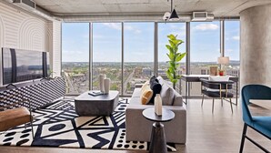 Un salon moderne doté d’un grand téléviseur, d’un canapé, d’une table basse et d’un coin repas offrant une vue sur la ville.