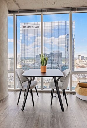 A modern office space with a large window, a table with two chairs, a potted plant, and a woven basket. - Work-Ready Downtown Stay | Rooftop Lounge & Kitchen | Near Broadway & Symphony (Nashville)