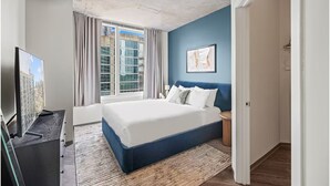 Ein Schlafzimmer mit einem großen Bett, einem Fernseher, einem Fenster mit Vorhängen und einer blauen Akzentwand.