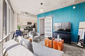 Ein modernes Wohnzimmer mit Sofa, Couchtisch, Fernseher und einer Schiebetür zum Küchenbereich.