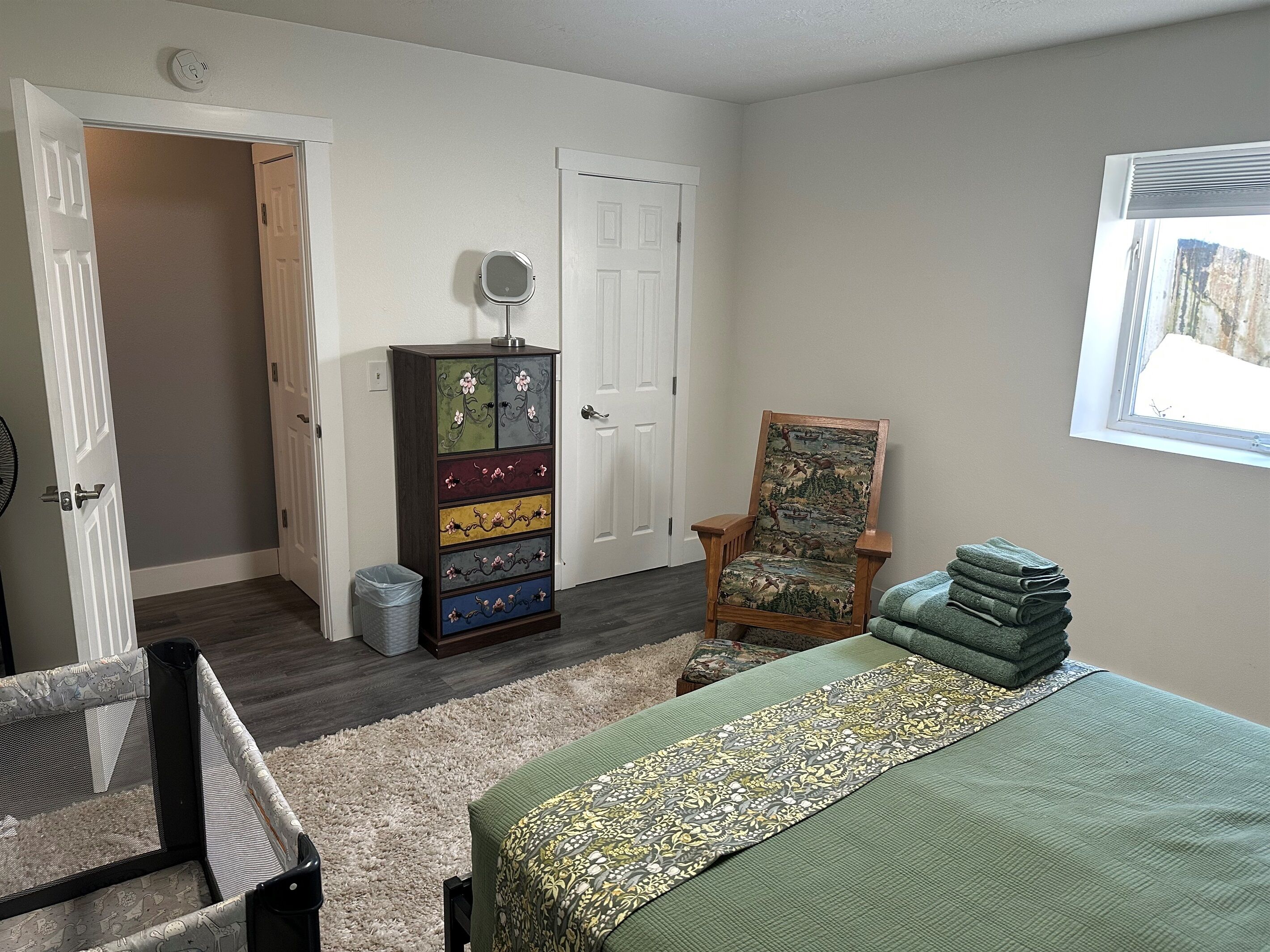 Une chambre à coucher avec un lit, une commode, une chaise, une fenêtre et une porte.