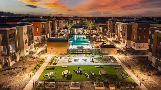 A modern apartment complex with a central swimming pool, outdoor seating, and a well-maintained lawn.