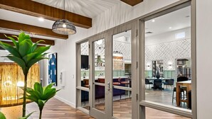 A modern interior with a wooden floor, a dining area with chairs, and a kitchen visible through glass doors.
