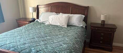 A neatly made bed with a floral-patterned bedspread, two bedside tables with lamps, and a wooden nightstand with drawers.