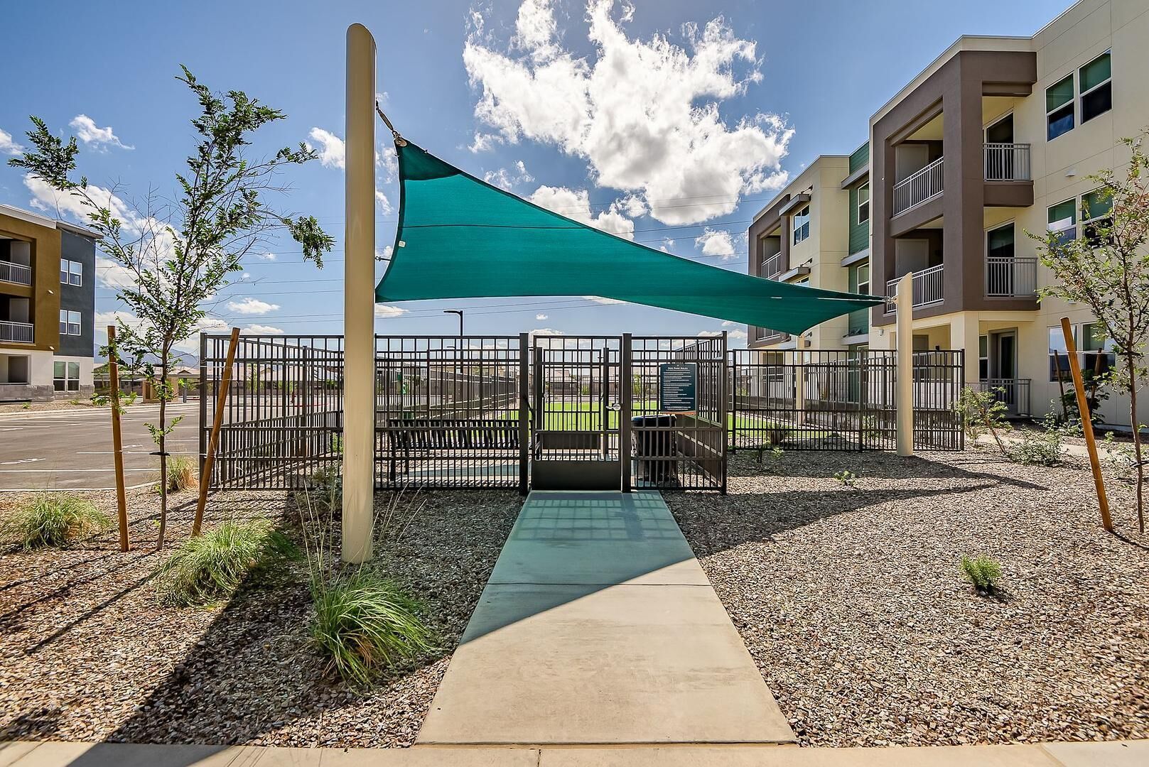 A gated outdoor area with a pathway leading to a building entrance, surrounded by gravel and small plants.