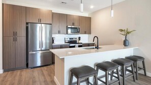A modern kitchen with a stainless steel refrigerator, a microwave, and an oven. There are wooden cabinets and a white countertop. - Landing | Beautiful 2BD, Pool, Gym (Goodyear)