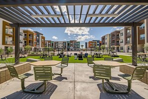 A courtyard with outdoor seating, a pool, and apartment buildings in the background. - Landing | Spectacular 2BD, Pool, Clubhouse (Goodyear)