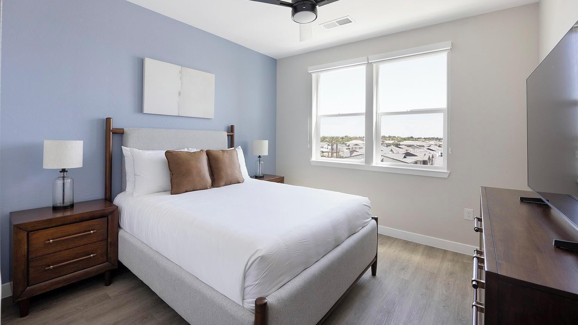 A bedroom with a bed, nightstands, a TV, and a window with a view.