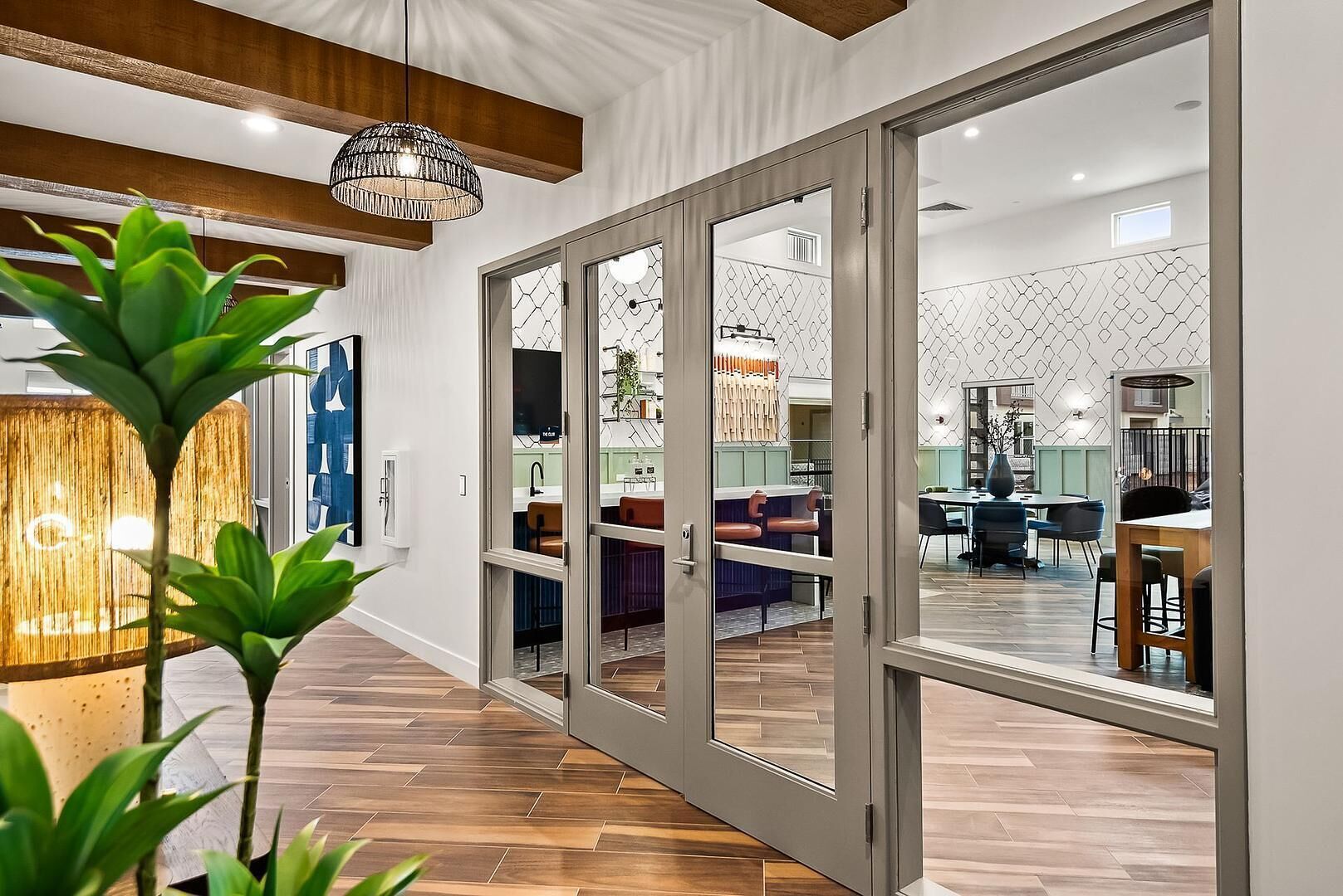 A modern interior with a wooden floor, a dining area with chairs, and a kitchen visible through glass doors.